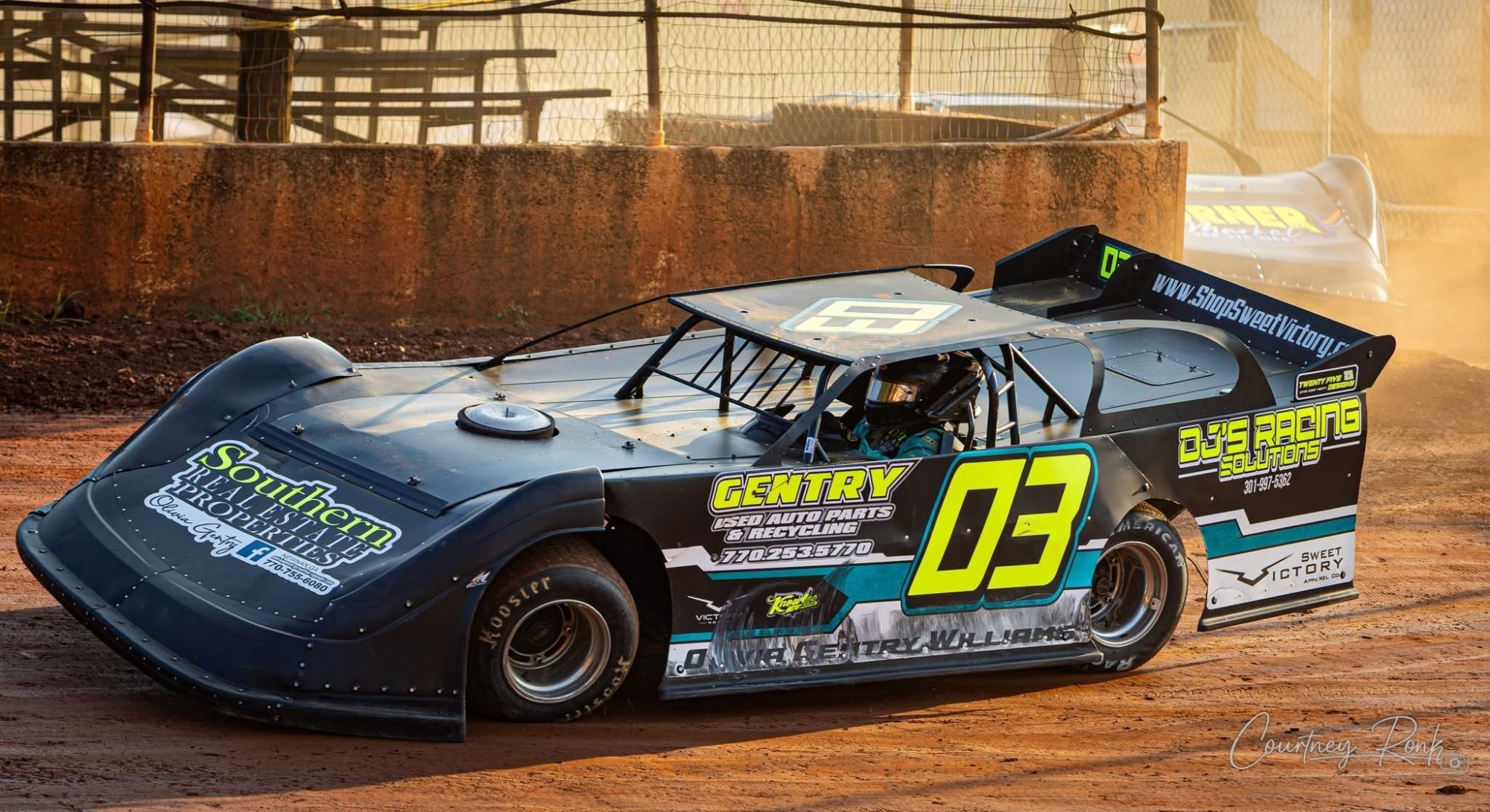 Olivia Gentry Williams racing her black #03 dirt late model, branded with Southern Real Estate Properties, on a red clay track