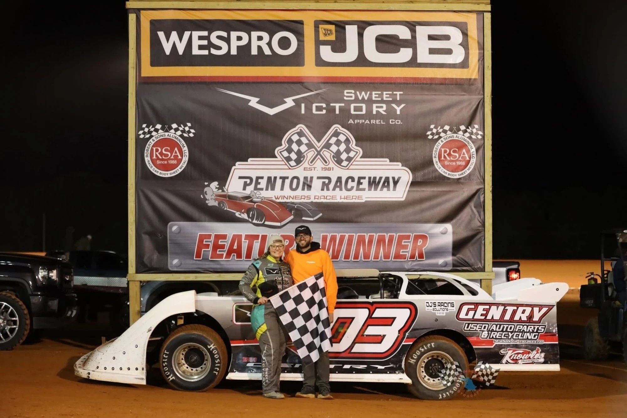 Olivia Gentry Williams holding the checkered flag beside her #03 dirt late model after a feature win at Penton Raceway