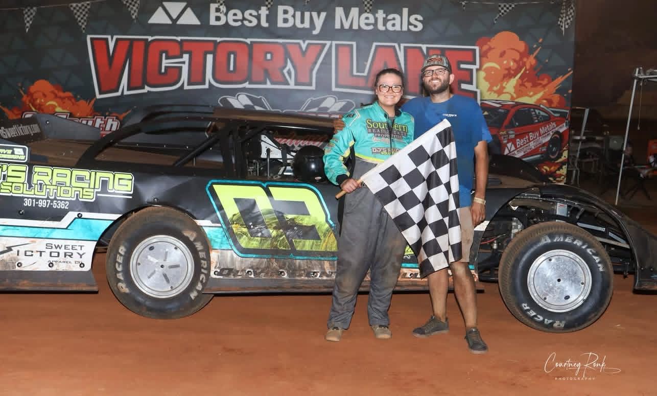 Olivia Gentry Williams holding the checkered flag in Victory Lane beside her #03 dirt late model